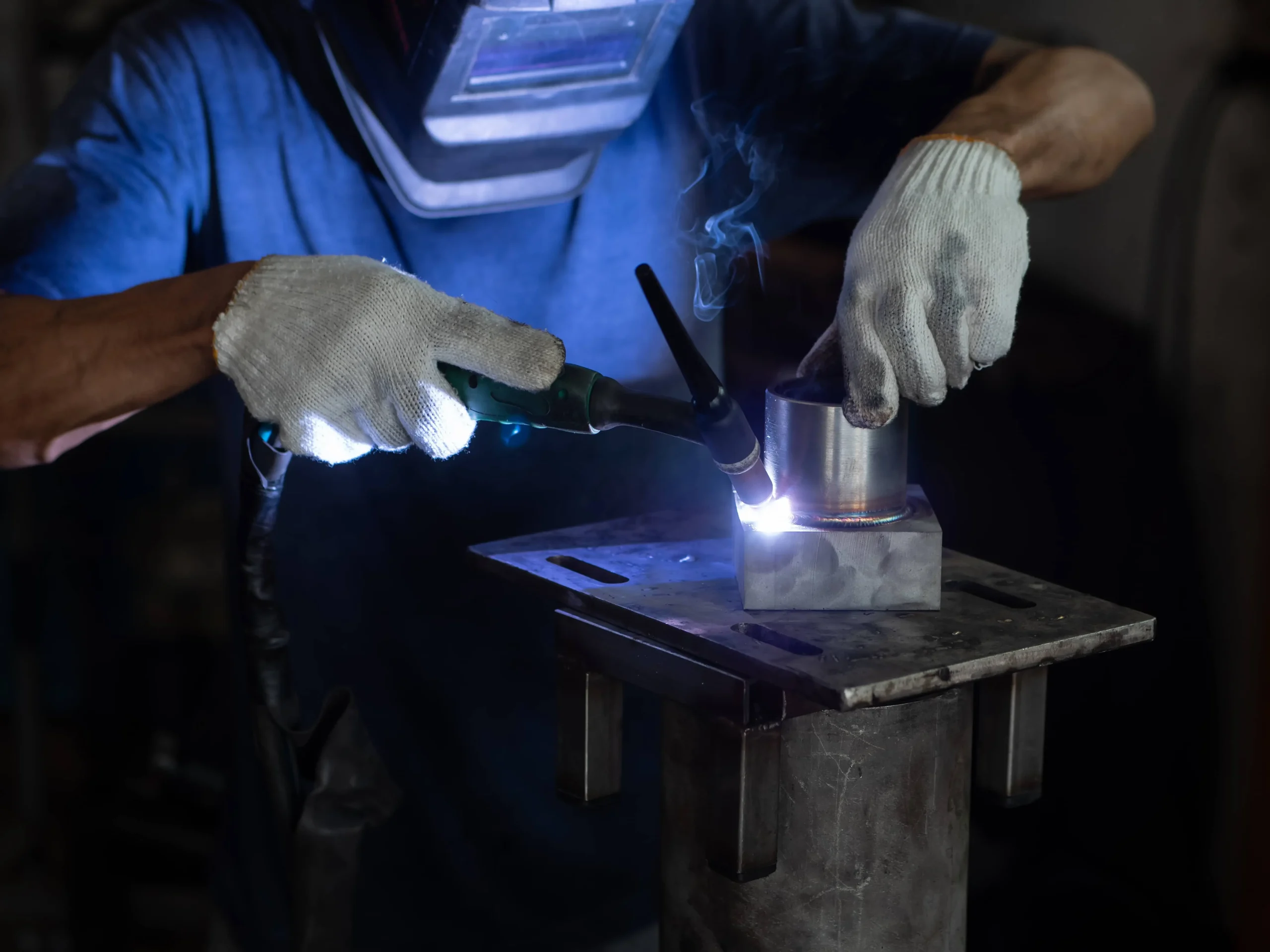 Un soudeur équipé d’un masque et de gants de protection assemble deux pièces métalliques à l’aide du procédé MIG.