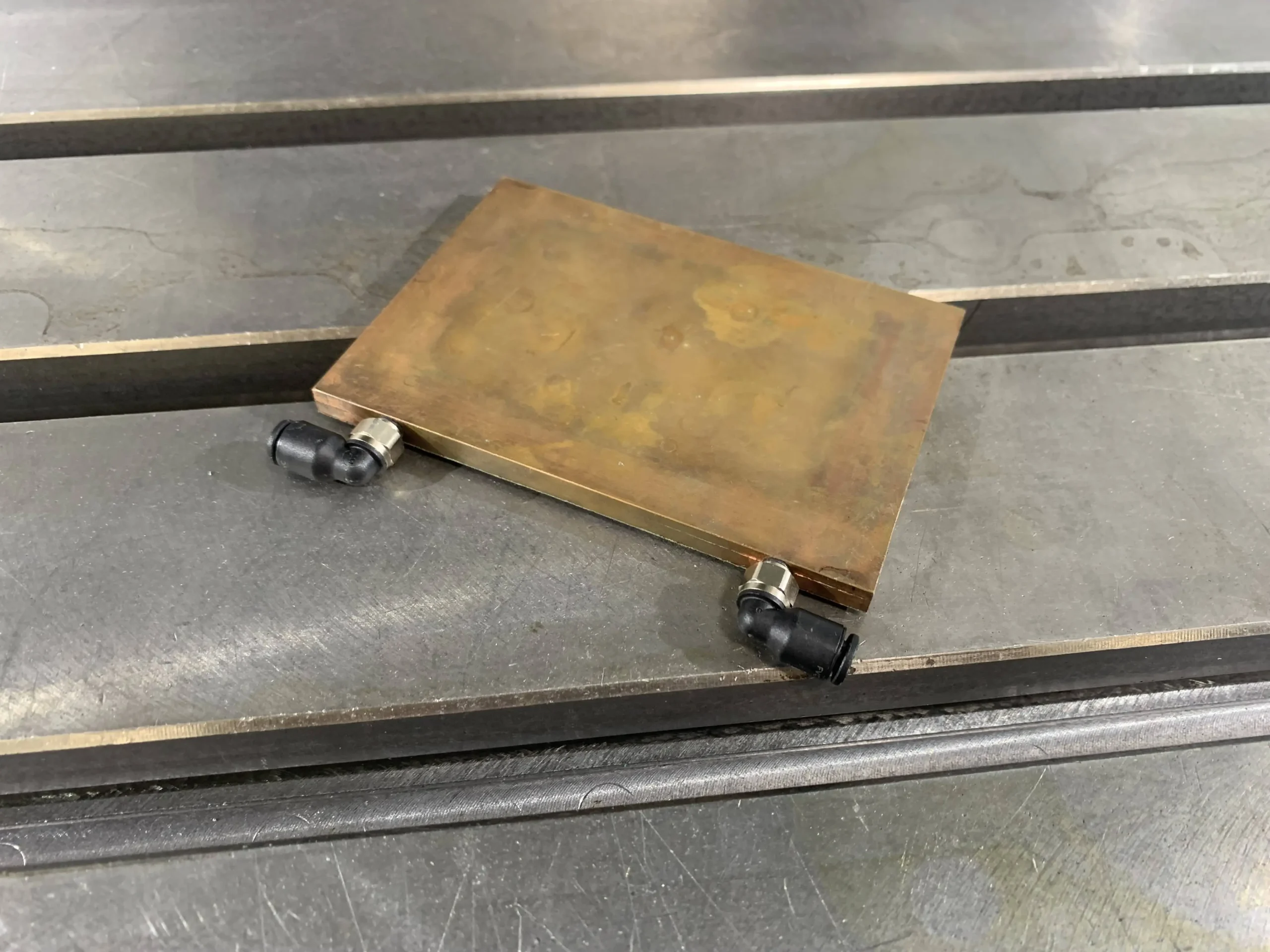 Conjunto de placa de refrigeración de cobre equipado con conectores de entrada y salida, que presenta una superficie plana sellada para aplicaciones de refrigeración por líquido.