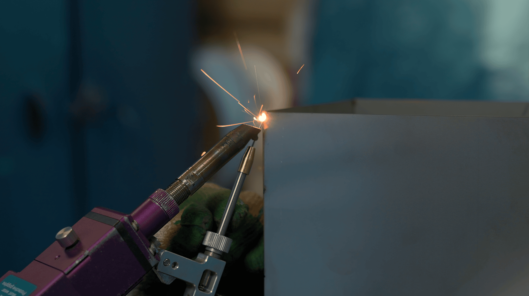 Cabezal de soldadura láser que une el borde de un componente metálico, con chispas visibles y una zona de fusión muy localizada.